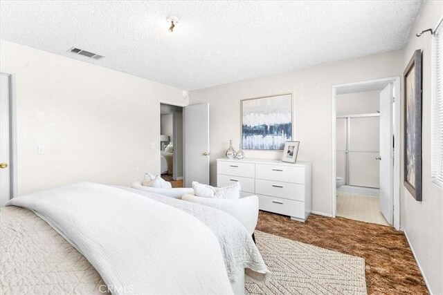 carpeted bedroom with connected bathroom, multiple windows, a textured ceiling, and visible vents
