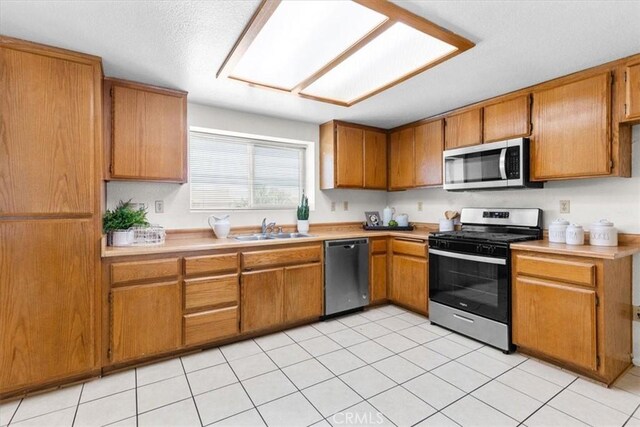 kitchen with brown cabinetry, appliances with stainless steel finishes, a sink, and light countertops