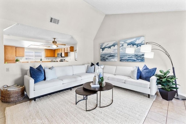 living area featuring vaulted ceiling, visible vents, light tile patterned flooring, a textured ceiling, and ceiling fan