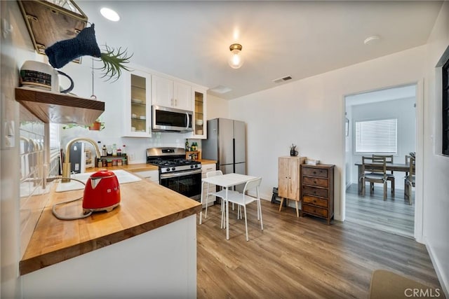 kitchen with wood finished floors, white cabinets, a sink, wood counters, and stainless steel appliances