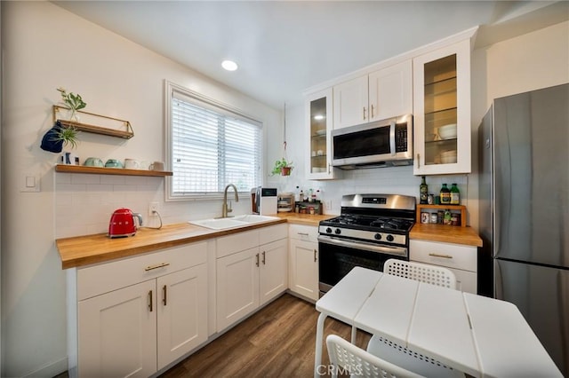 kitchen with decorative backsplash, dark wood-style flooring, butcher block countertops, a sink, and appliances with stainless steel finishes
