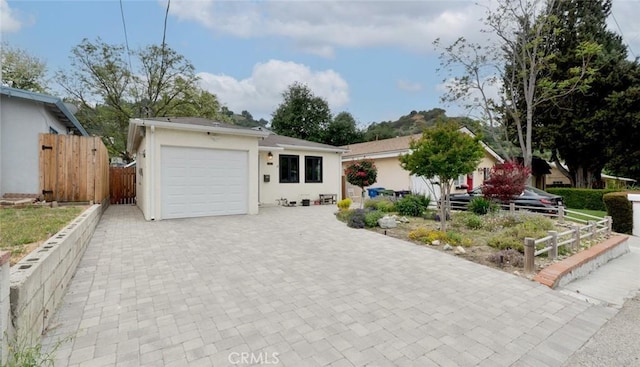 ranch-style house featuring decorative driveway, an attached garage, fence, and stucco siding