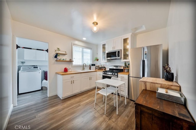 kitchen with appliances with stainless steel finishes, a sink, light wood-style floors, white cabinetry, and glass insert cabinets