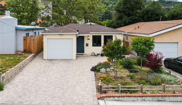 ranch-style home featuring fence, roof with shingles, a garage, stucco siding, and decorative driveway