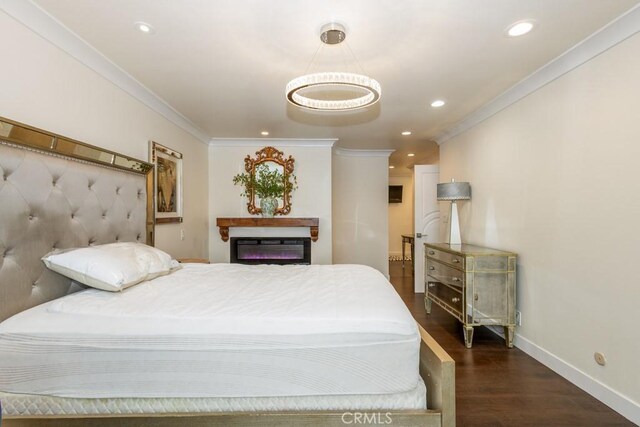 bedroom with crown molding, wood finished floors, baseboards, a glass covered fireplace, and recessed lighting