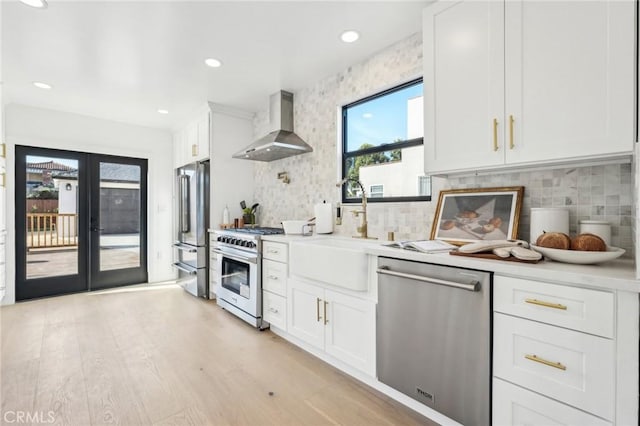 kitchen featuring high end appliances, wall chimney exhaust hood, light countertops, and decorative backsplash