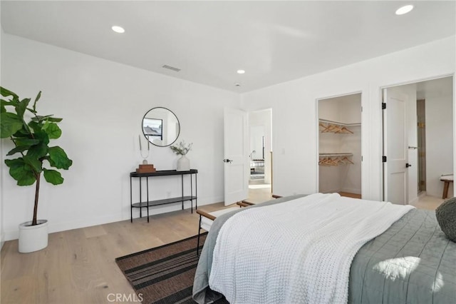 bedroom with baseboards, visible vents, recessed lighting, wood finished floors, and a walk in closet