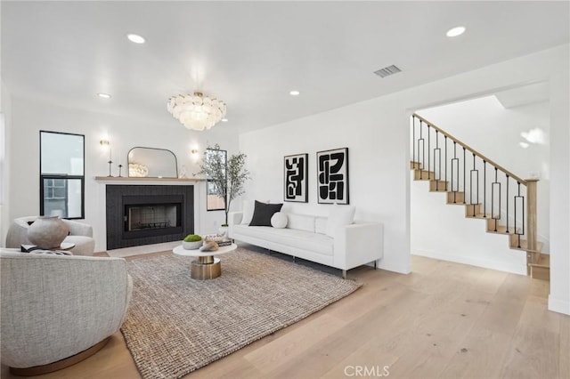 living area featuring a fireplace with flush hearth, light wood-style flooring, visible vents, recessed lighting, and stairway