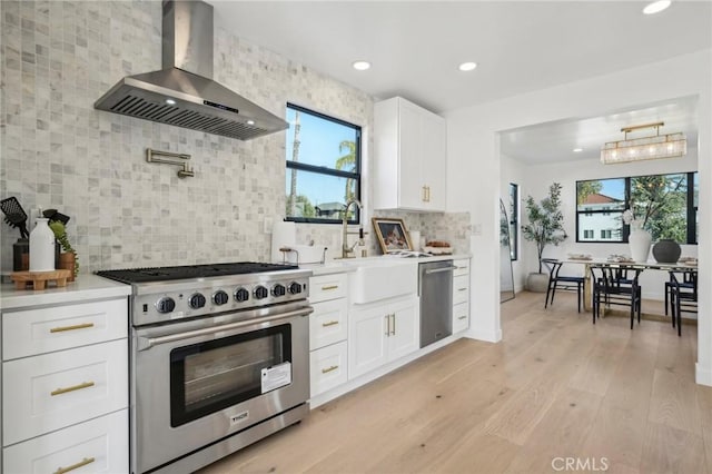 kitchen featuring decorative backsplash, light countertops, appliances with stainless steel finishes, and wall chimney range hood