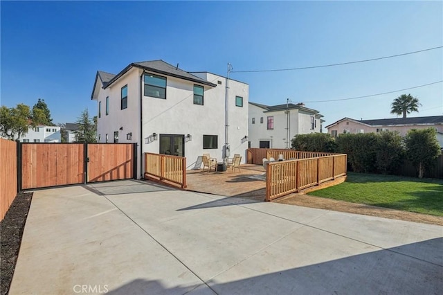 rear view of house featuring a gate, fence private yard, a lawn, a patio, and stucco siding