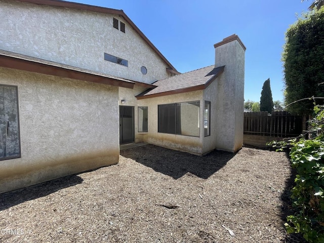 rear view of property with a chimney, stucco siding, and fence
