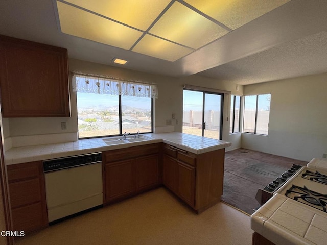kitchen with tile counters, white dishwasher, a sink, open floor plan, and a peninsula