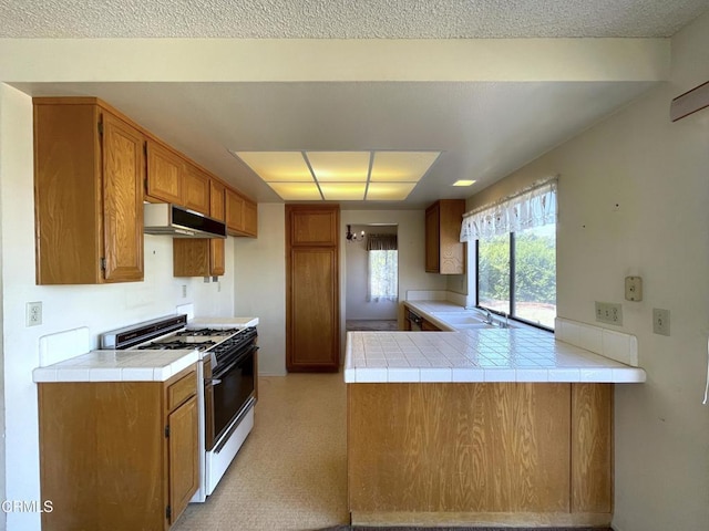 kitchen with a peninsula, a sink, range with gas stovetop, exhaust hood, and brown cabinets