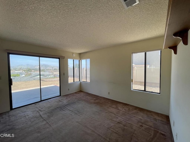 spare room with a textured ceiling, carpet flooring, and visible vents