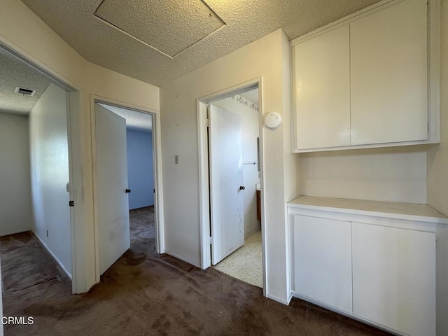 corridor featuring attic access, a textured ceiling, carpet floors, and visible vents