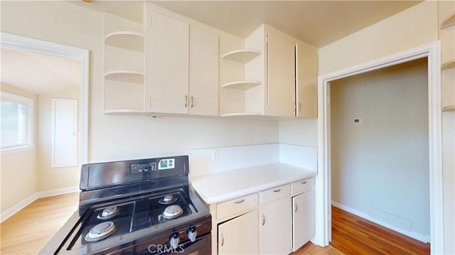 kitchen featuring open shelves, white cabinets, light wood-style flooring, black gas stove, and light countertops