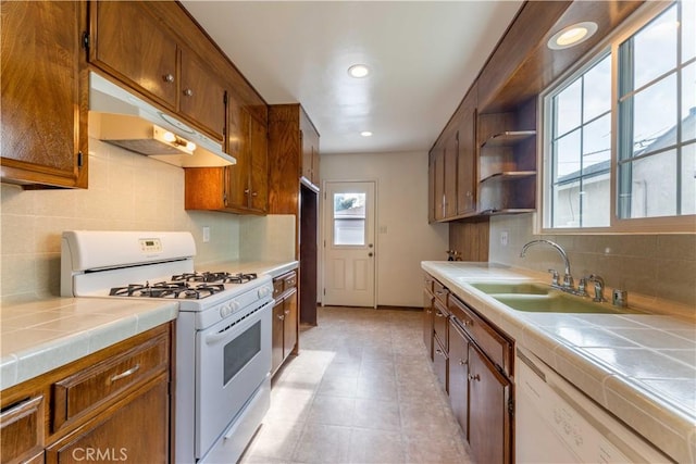 kitchen featuring a sink, under cabinet range hood, tile countertops, white appliances, and backsplash