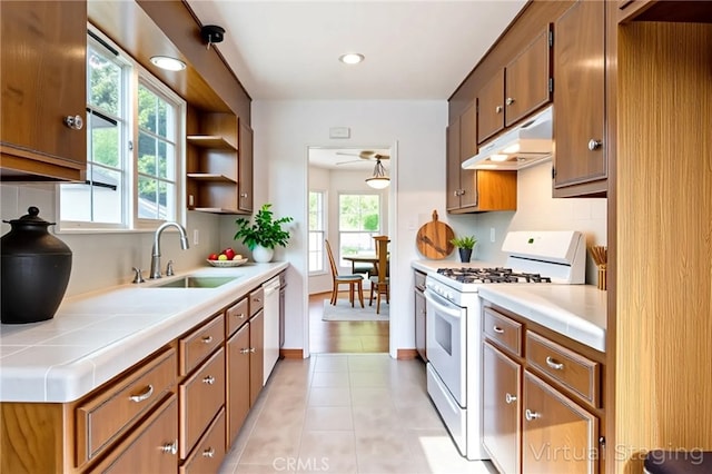 kitchen featuring a sink, white appliances, brown cabinets, under cabinet range hood, and light tile patterned floors