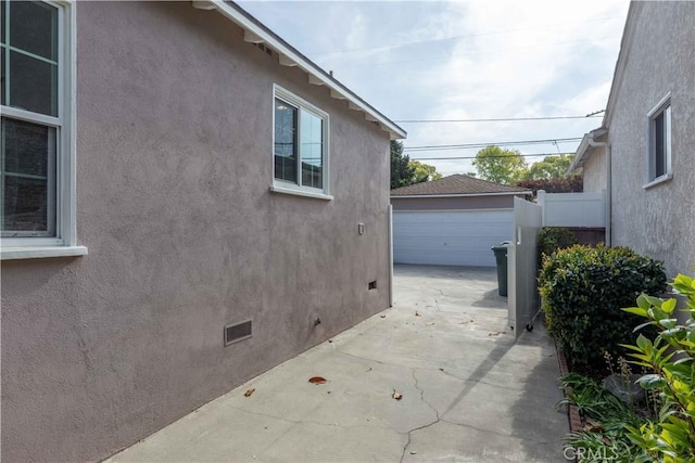 view of side of home featuring crawl space, a detached garage, an outdoor structure, fence, and stucco siding