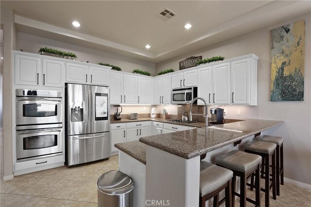 kitchen with a peninsula, light tile patterned flooring, visible vents, white cabinetry, and appliances with stainless steel finishes