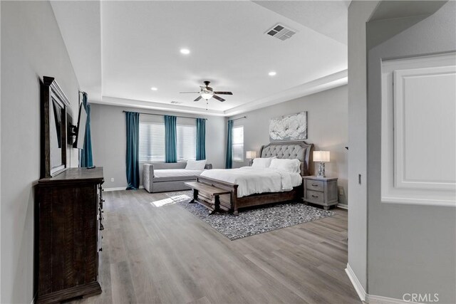 bedroom with a tray ceiling, light wood-type flooring, visible vents, and baseboards
