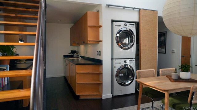 laundry area featuring a sink, stacked washer and clothes dryer, baseboards, dark wood-type flooring, and laundry area