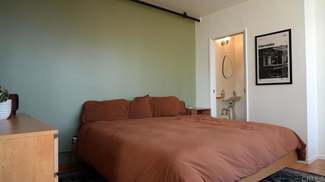 bedroom with a barn door, baseboards, and wood finished floors