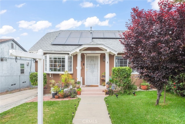 bungalow-style house featuring a shingled roof, roof mounted solar panels, and a front lawn