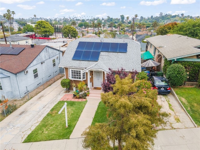 view of front facade featuring driveway, solar panels, a front yard, a residential view, and a shingled roof