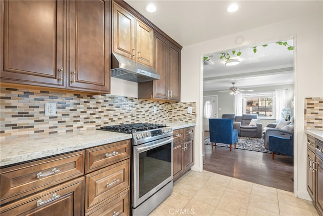 kitchen with open floor plan, stainless steel gas range oven, under cabinet range hood, a ceiling fan, and backsplash
