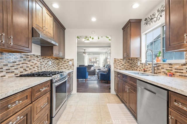 kitchen featuring ceiling fan, backsplash, a sink, under cabinet range hood, and stainless steel appliances