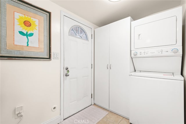 clothes washing area with light tile patterned floors, stacked washer and clothes dryer, and cabinet space