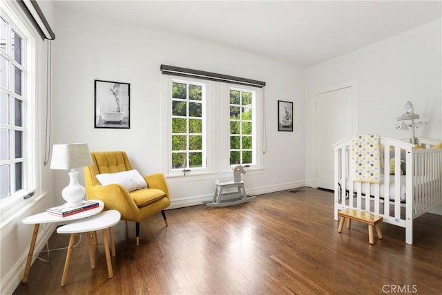 bedroom featuring a nursery area, baseboards, and wood finished floors
