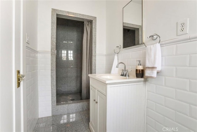 full bath featuring tile walls, granite finish floor, vanity, and a wainscoted wall