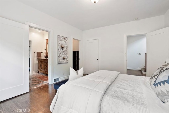 bedroom with wood finished floors, visible vents, baseboards, and connected bathroom