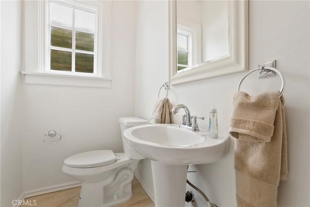 half bathroom featuring wood finished floors, baseboards, a wealth of natural light, and toilet