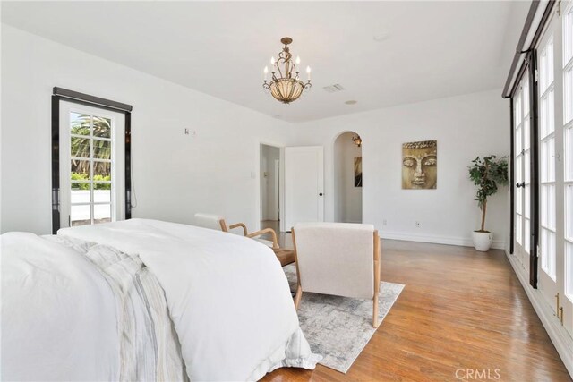 bedroom featuring light wood-style flooring, arched walkways, baseboards, visible vents, and a chandelier