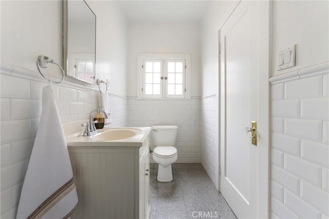 bathroom with tile walls, a wainscoted wall, vanity, and toilet