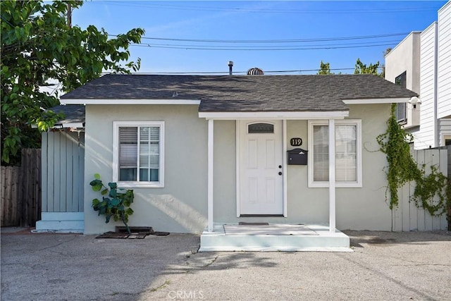 view of front facade featuring stucco siding, fence, and roof with shingles