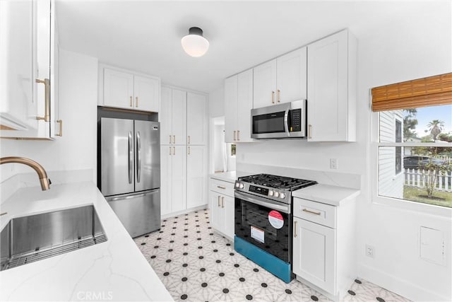 kitchen featuring light stone countertops, white cabinetry, stainless steel appliances, and a sink