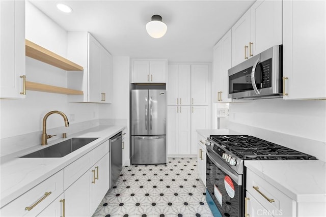 kitchen with a sink, white cabinetry, open shelves, light stone countertops, and appliances with stainless steel finishes