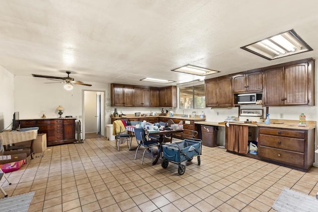 kitchen with dark brown cabinets, light countertops, stainless steel microwave, and light tile patterned flooring