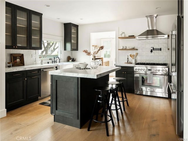 3702 Seneca Ave, Los Angeles, CA 90039 - kitchen featuring light wood finished floors, stainless steel appliances, dark cabinets, wall chimney range hood, and tasteful backsplash