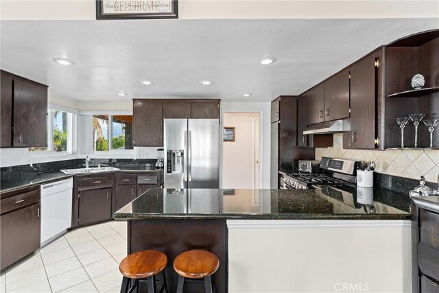 kitchen featuring stainless steel appliances, a peninsula, a sink, dark brown cabinetry, and under cabinet range hood