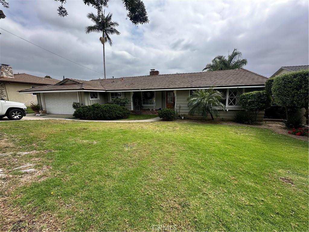 single story home featuring concrete driveway, an attached garage, a chimney, and a front yard