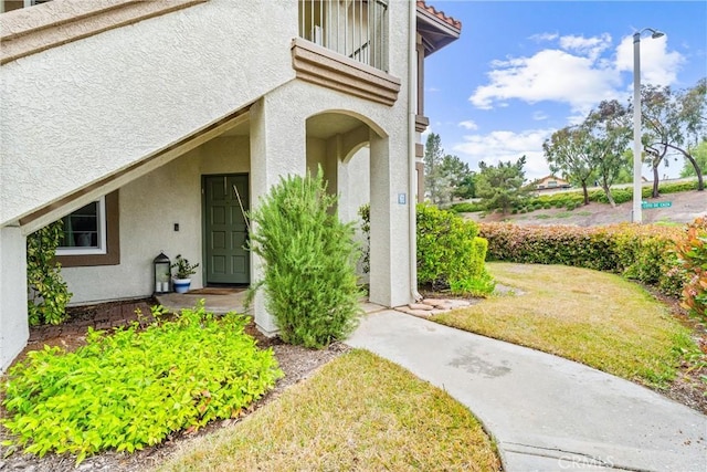 doorway to property with a lawn and stucco siding
