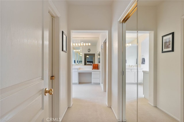hall with light colored carpet and an inviting chandelier