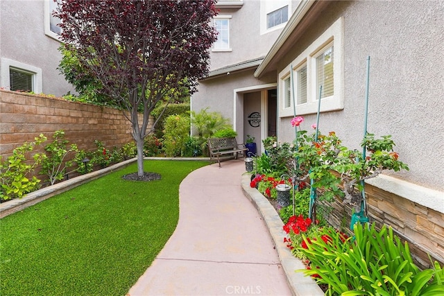 entrance to property featuring a lawn, fence, and stucco siding