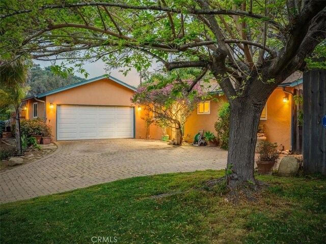 ranch-style house with an attached garage, a front lawn, decorative driveway, and stucco siding