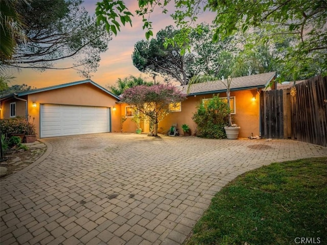 single story home featuring an attached garage, fence, decorative driveway, and stucco siding